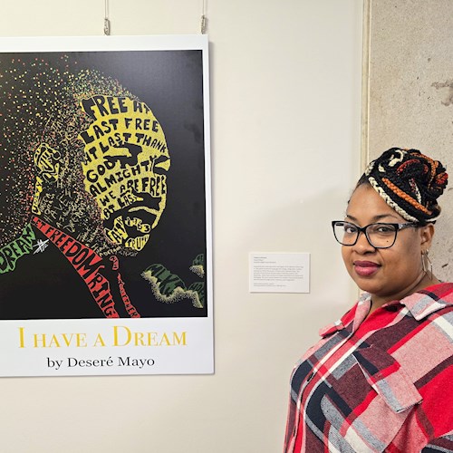 Woman in glasses and red plaid shirt standing beside a digital artwork titled “I HAVE A DREAM” by Deseré Mayo. The piece features a stylized profile of Martin Luther King Jr. formed from colorful typography, including phrases like “FREE AT LAST,” “FREEDOM