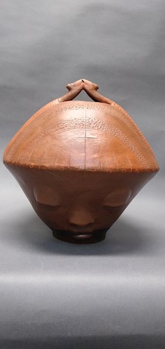 Ceramic sculpture that is a medium reddish-brown color with eyes, nose and mouth and a serene expression