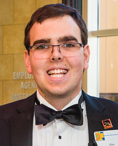 Image of a smiling man with brown hair and glasses wearing a black tuxedo, white shirt, and black bowtie