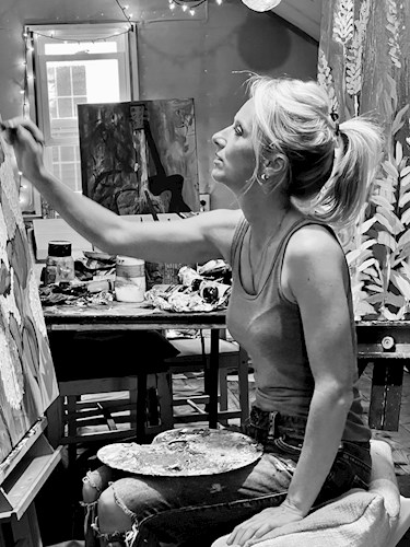 Black and white image of a blonde woman with a ponytail painting at a canvas in an art studio