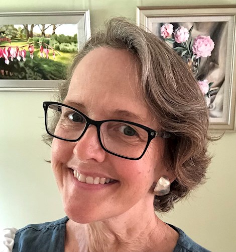 Close up image of smiling woman with short brown and grey hair, black glasses and a silver earring