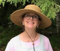 Photo of a smiling woman wearing glasses, a sun hat, and a pink top.