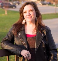 Photo of a smiling woman with long dark brown hair, wearing a black leather jacket.