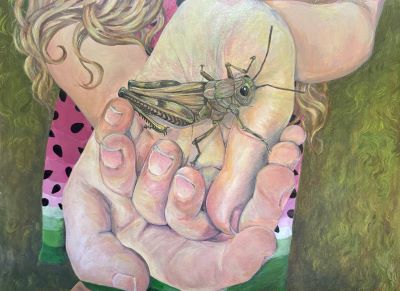 A child’s hands gently holding a large grasshopper. The child wears a pink shirt with black spots and has long, curly blonde hair. Green foliage in the background suggests an outdoor setting.